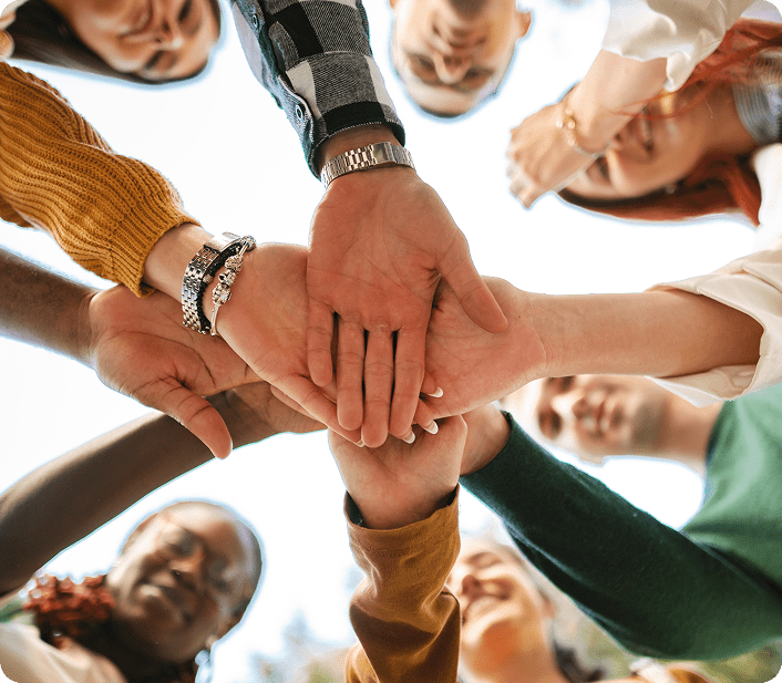 Group of diverse people joining hands in unity, viewed from below.