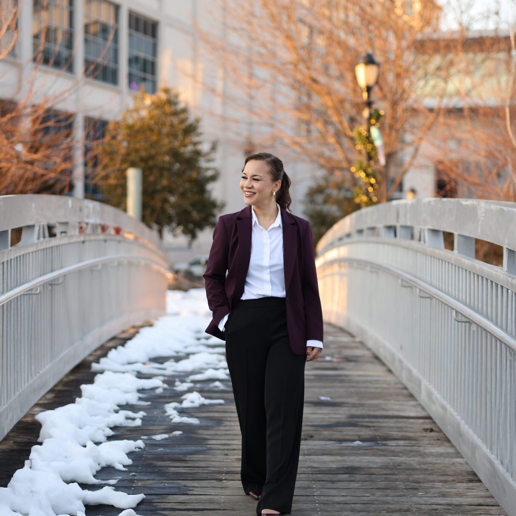 A woman in business attire walking on a snowy bridge outdoors.